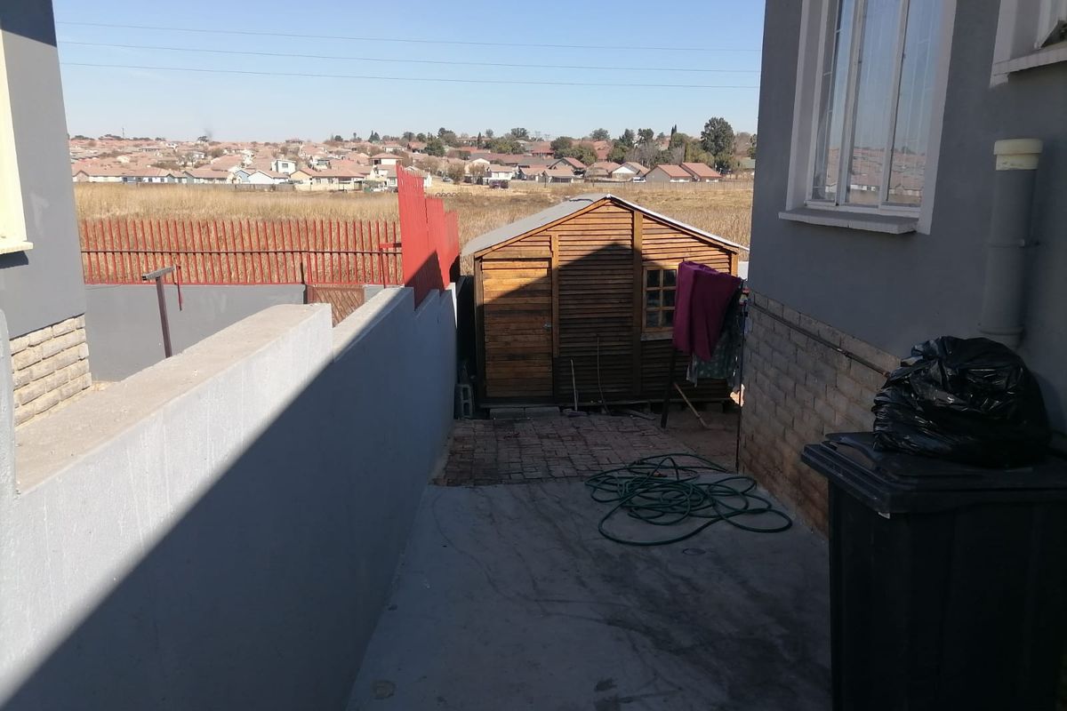 A side exterior view of the property featuring a paved walkway, a wooden storage shed, and perimeter boundary walls.