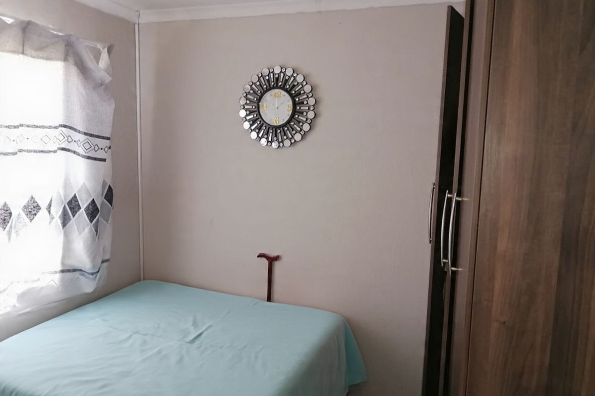 A compact bedroom featuring a built-in wooden wardrobe and a window with natural light.
