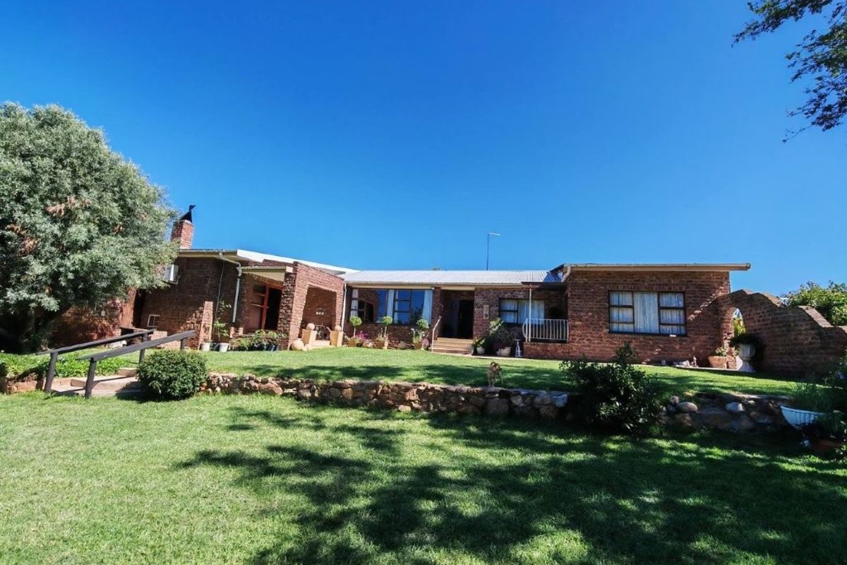 A rear view of a face brick farmhouse featuring a corrugated metal roof, a stone retaining wall, and a spacious lawn area.