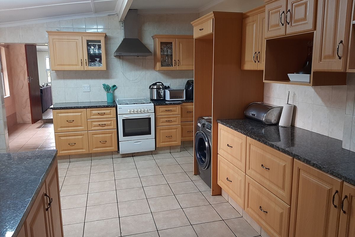 A functional kitchen featuring light wood cabinetry, granite countertops, tiled flooring, and a built-in space for a washing machine.