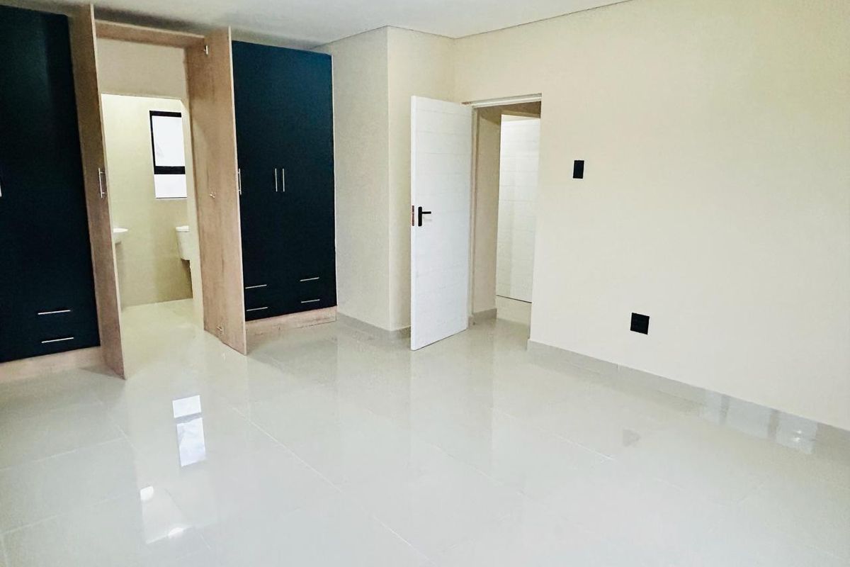 A bright, modern bedroom featuring polished tile flooring, built-in dark cabinetry, and an en-suite bathroom access.