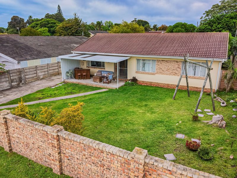 Rear view of a single-story house featuring a tiled roof, brick exterior, covered patio area, and a spacious private garden with boundary walling.