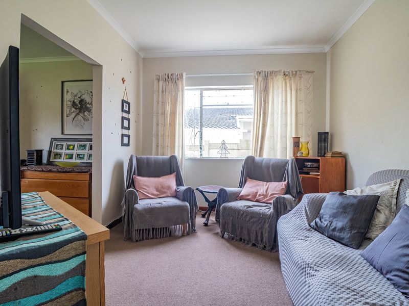 A living room area featuring carpet flooring, coving, and a window, showing signs of wear on the walls and flooring.