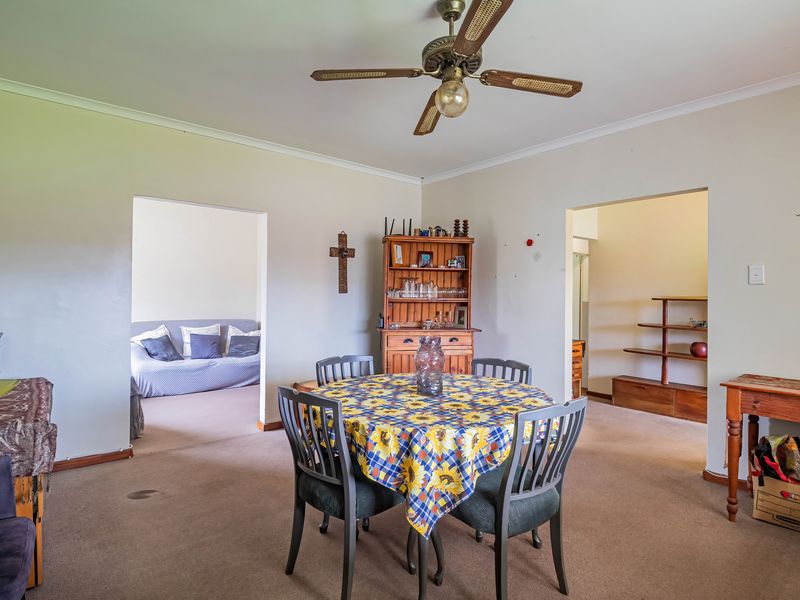 A living area featuring carpeted flooring, a ceiling fan, and coving, with open access to adjacent rooms.
