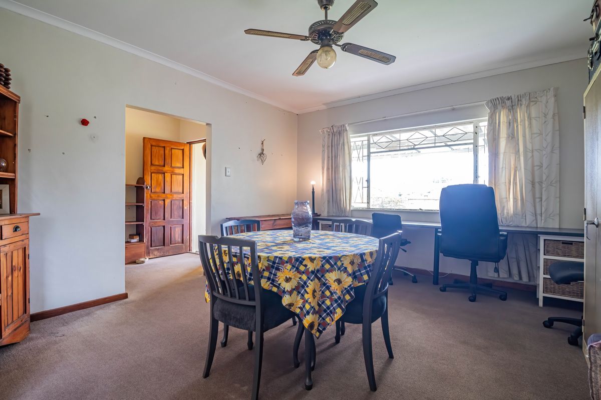 A multi-purpose living area featuring a ceiling fan, built-in desk space, and direct access to an adjacent room through a timber door.