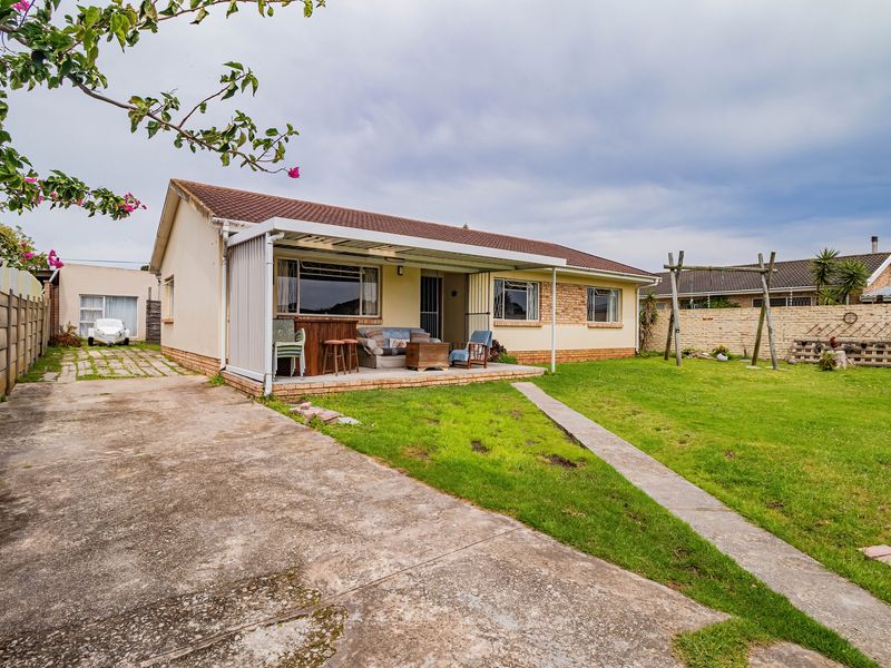 Rear view of the house featuring a covered patio, concrete driveway, and a spacious garden with a brick boundary wall.
