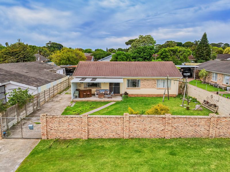 Aerial view of the rear exterior featuring a tiled roof house, a covered patio area, a spacious lawn, and a brick boundary wall.