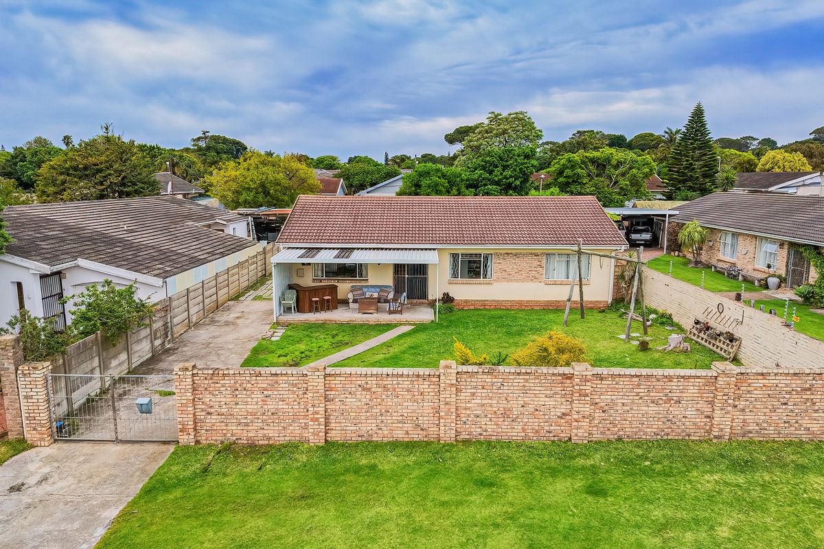 Aerial view of the rear exterior featuring a tiled roof house, a covered patio area, a spacious lawn, and a brick boundary wall.