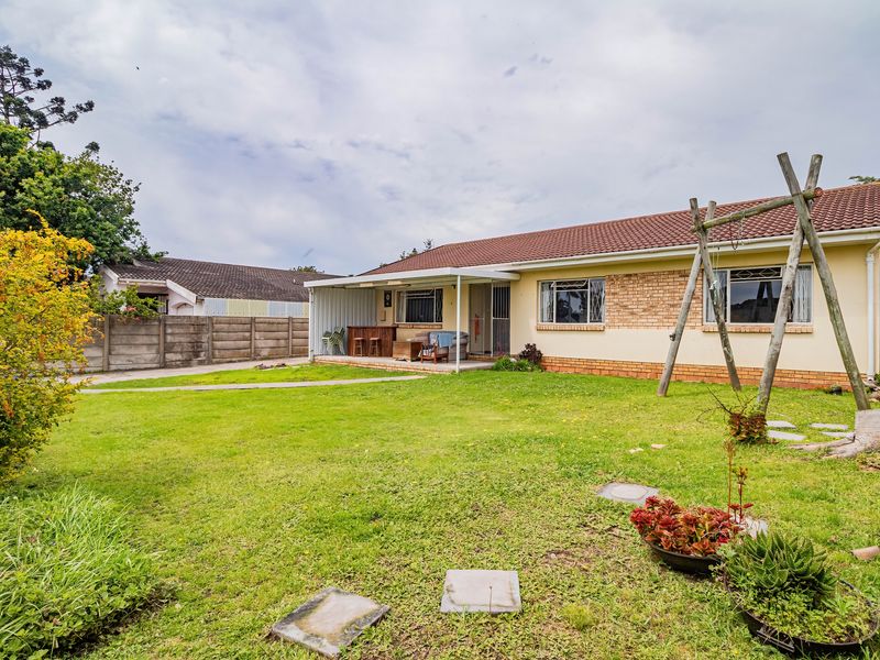 Rear view of the house featuring a spacious garden, a covered patio area, and a tiled roof with brick and plaster exterior finishes.