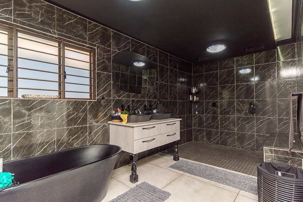 Modern bathroom featuring dark marble-effect wall tiling, a freestanding black bathtub, a double vanity with vessel sinks, and a spacious walk-in shower area.