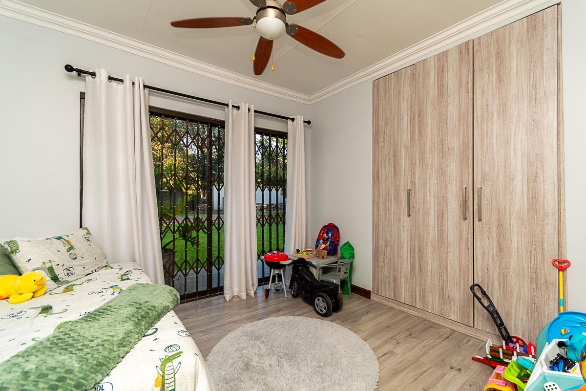 A well-maintained bedroom featuring built-in cupboards, laminate flooring, a ceiling fan, and sliding glass doors providing direct access to the garden.