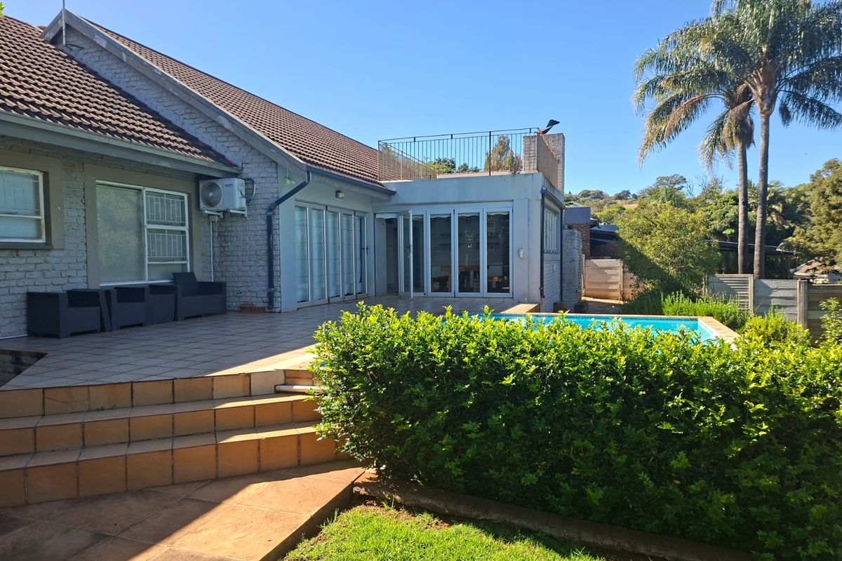 Rear view of the house featuring a tiled patio, swimming pool, and a rooftop balcony area with metal railings.