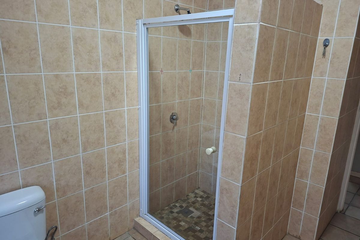 A functional bathroom featuring a tiled shower enclosure with a glass door and a standard toilet, finished with neutral ceramic wall and floor tiles.