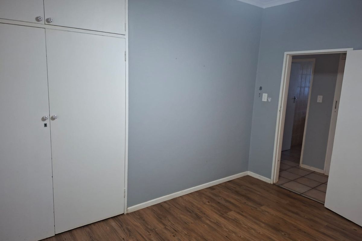 A bedroom featuring wood-look laminate flooring, built-in cupboards with overhead storage, and a doorway leading to an adjacent tiled room.