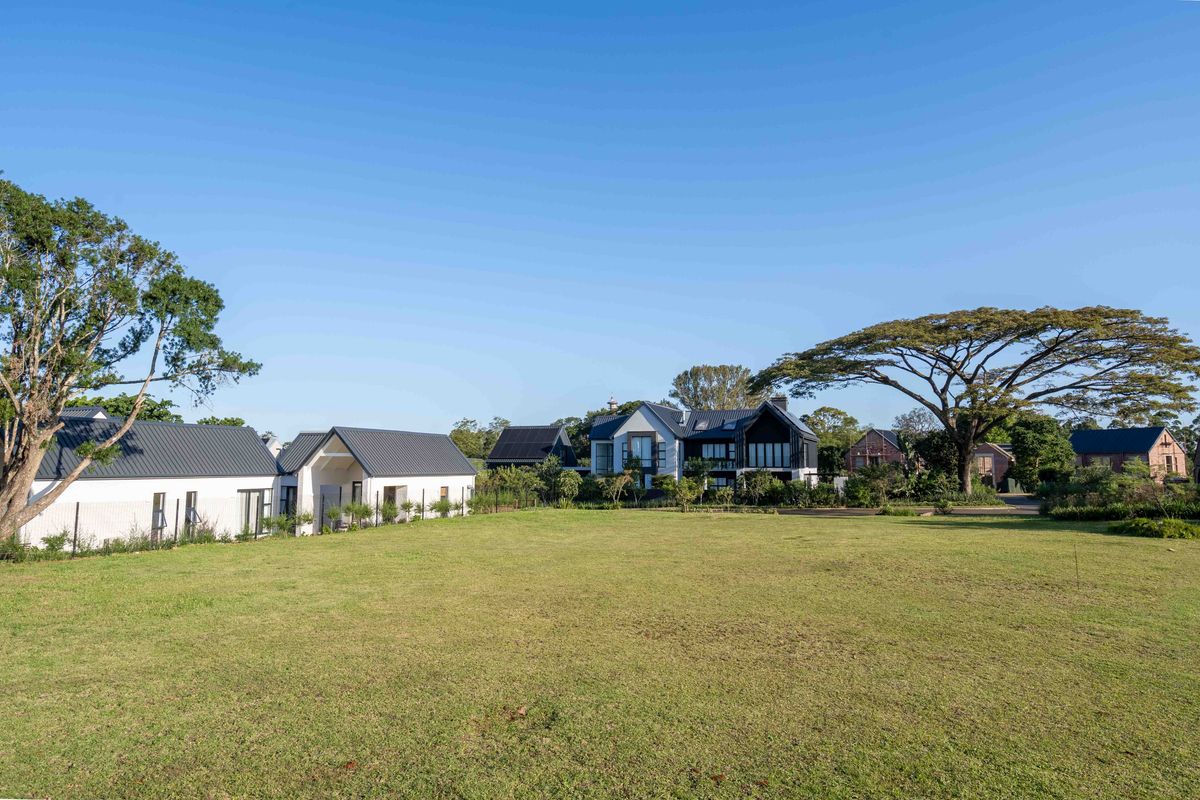 A wide-angle view of a spacious, well-maintained residential lawn with mature trees and neighboring modern homes in the background.