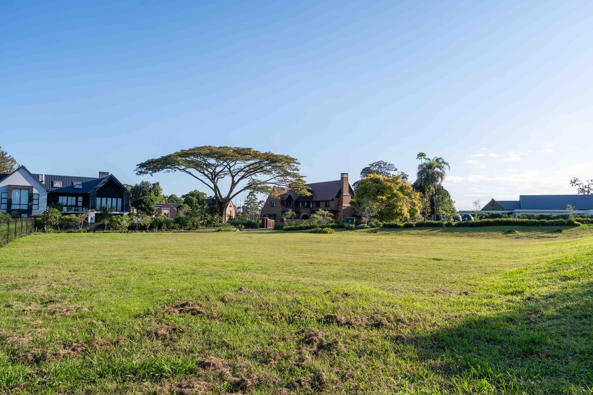 A spacious, well-maintained vacant residential plot featuring a level grass lawn, mature trees, and established perimeter fencing in a quiet neighborhood setting.