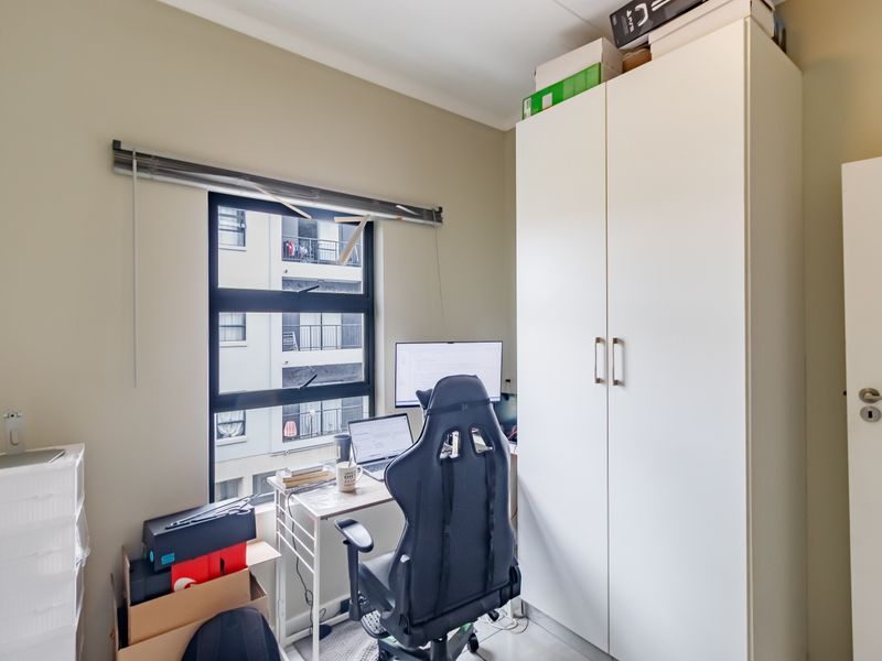 A compact bedroom featuring a built-in wardrobe and a window with an aluminium frame, currently utilized as a home office space.