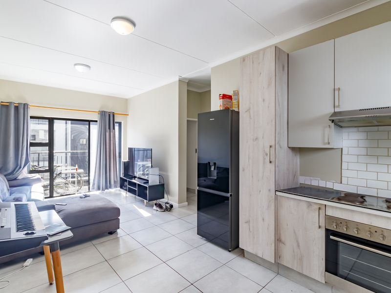 Open-plan living area featuring a modern kitchen with built-in appliances, tiled flooring, and a sliding glass door leading to a balcony.
