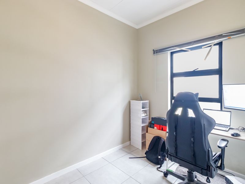 A functional office space featuring neutral wall tones, tiled flooring, and a large window with a fitted blind.