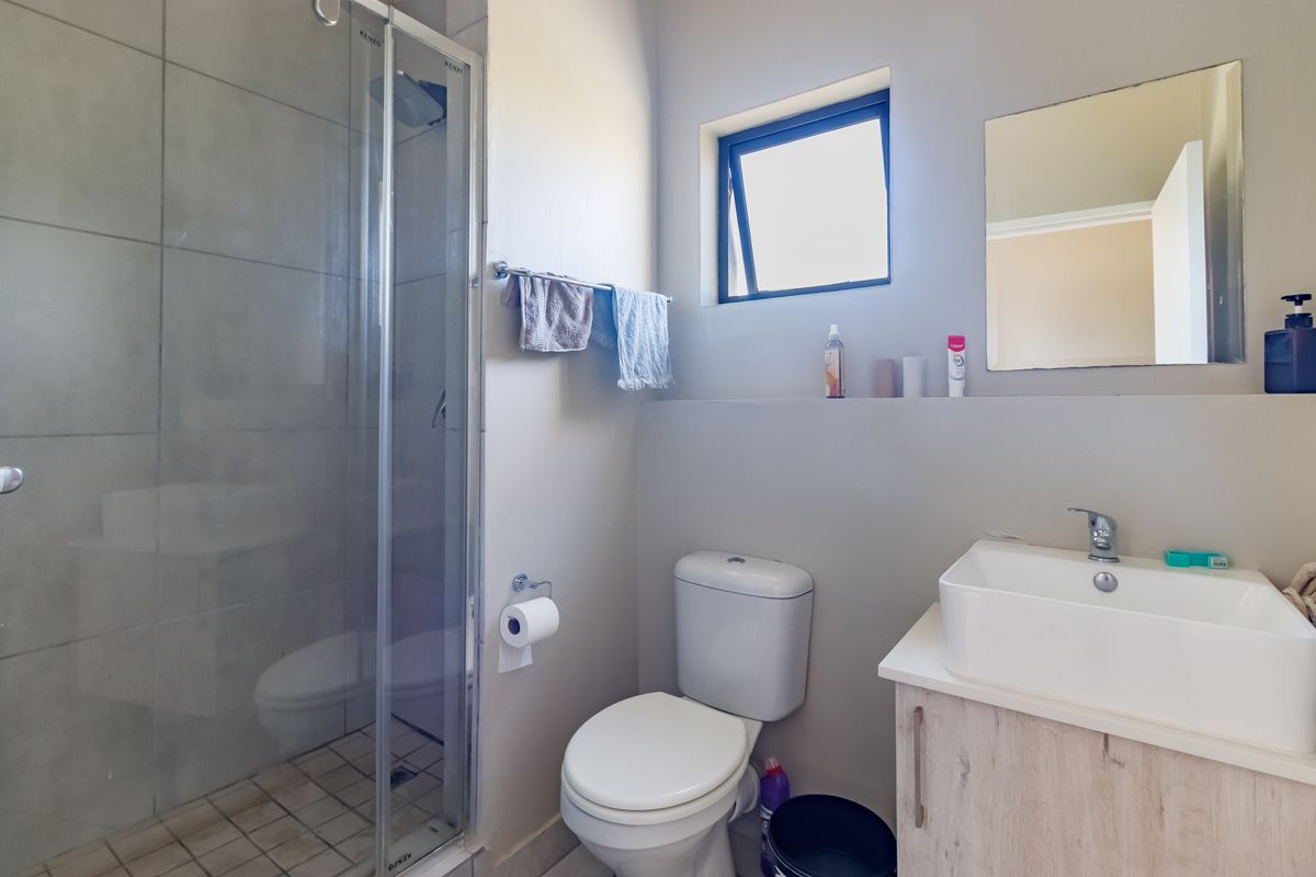 A functional bathroom featuring a glass-enclosed shower, a modern vessel sink with a vanity cabinet, and a wall-mounted toilet.