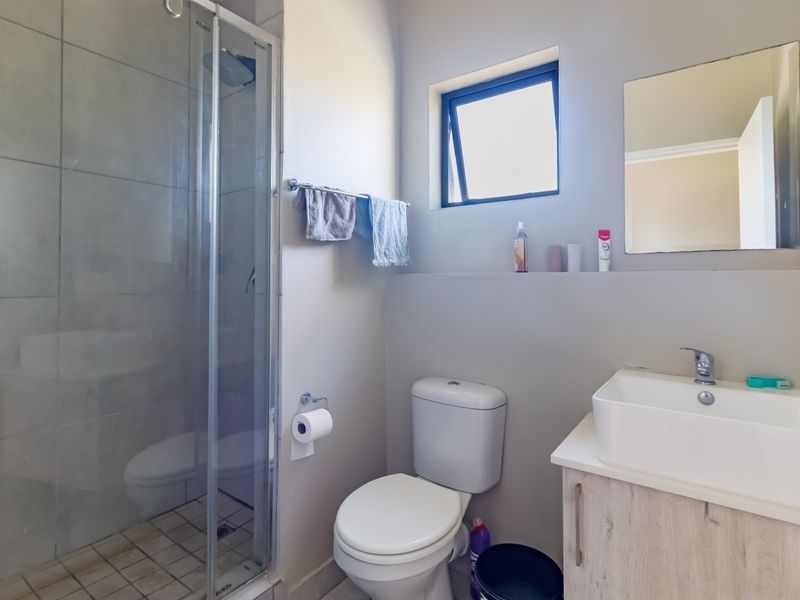 A functional bathroom featuring a glass-enclosed shower, a modern vessel sink with a vanity cabinet, and a wall-mounted toilet.