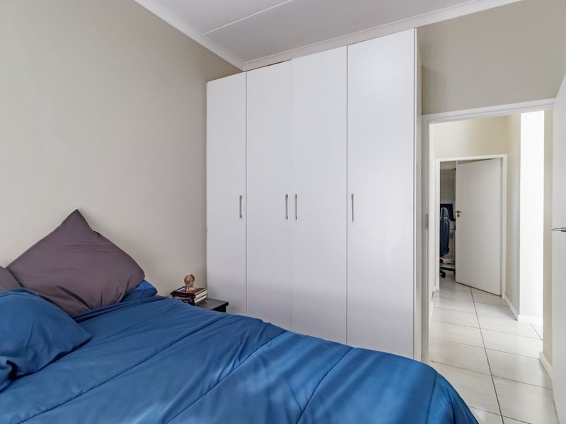 A well-maintained bedroom featuring a large white built-in wardrobe, neutral wall finishes, and tiled flooring leading to an adjacent hallway.