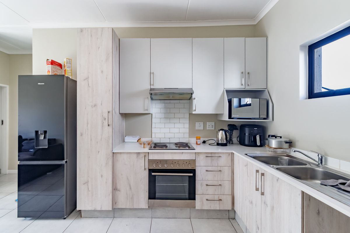 Modern kitchen featuring light wood-grain cabinetry, subway tile backsplash, integrated oven and hob, and a double bowl sink with ample storage space.