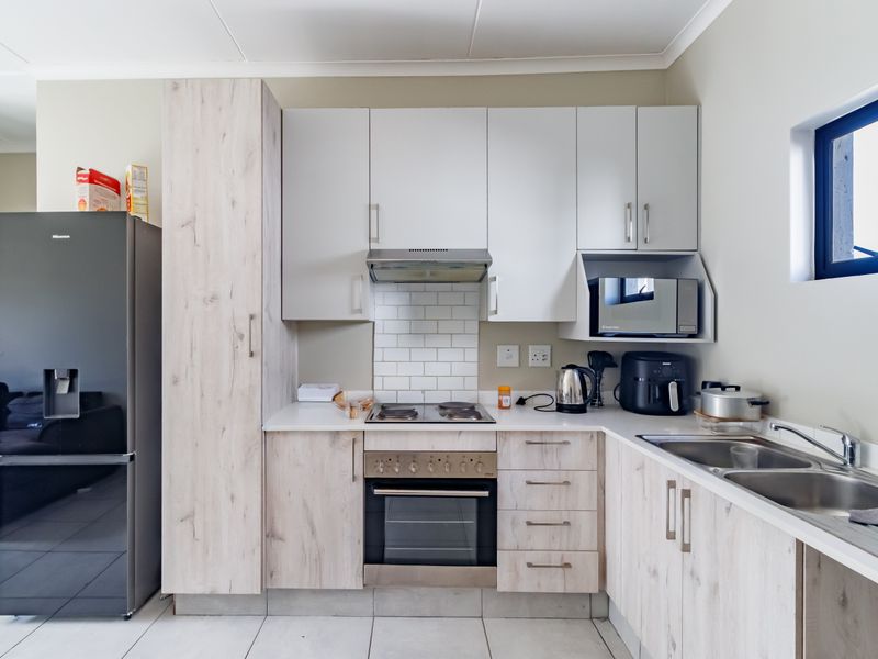 Modern kitchen featuring light wood-grain cabinetry, subway tile backsplash, integrated oven and hob, and a double bowl sink with ample storage space.