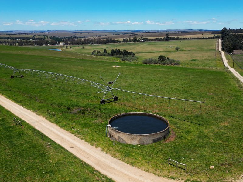 Aerial view of a farm property featuring a center pivot irrigation system, a concrete water reservoir, and surrounding agricultural land with access roads.