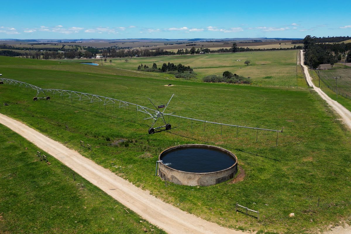 Aerial view of a farm property featuring a center pivot irrigation system, a concrete water reservoir, and surrounding agricultural land with access roads.