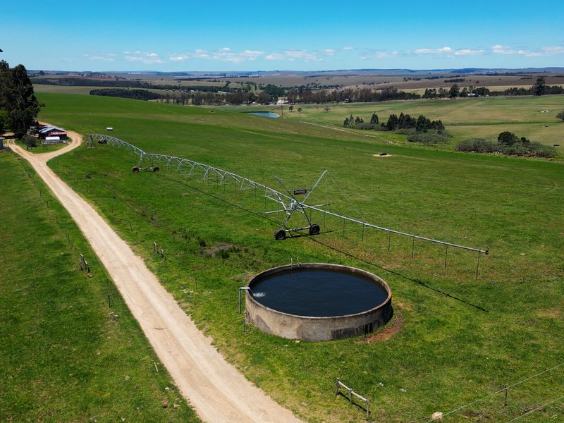 Aerial view of a farm property featuring a large center pivot irrigation system, a concrete water reservoir, and an extensive gravel access road.