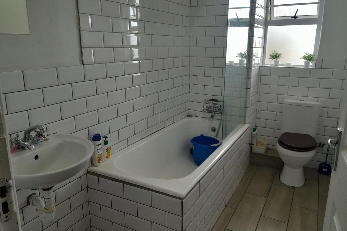 A clean bathroom featuring white subway tile walls, a bathtub with a glass shower screen, a pedestal basin, and a toilet.