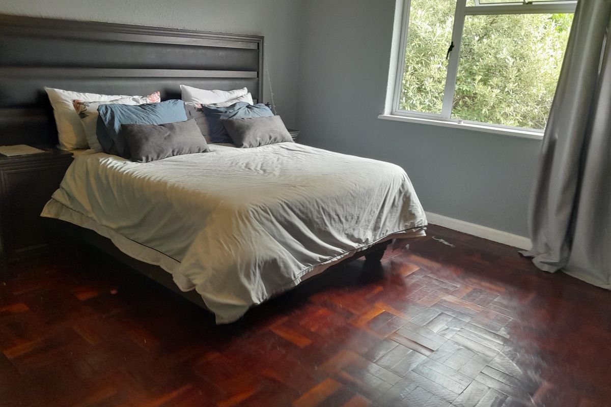 A bedroom featuring dark parquet flooring, a large window with natural light, and neutral wall tones.