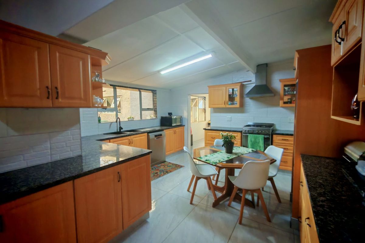 Spacious kitchen featuring wooden cabinetry, granite countertops, tiled backsplash, and a dedicated dining area with integrated stove and extractor fan.