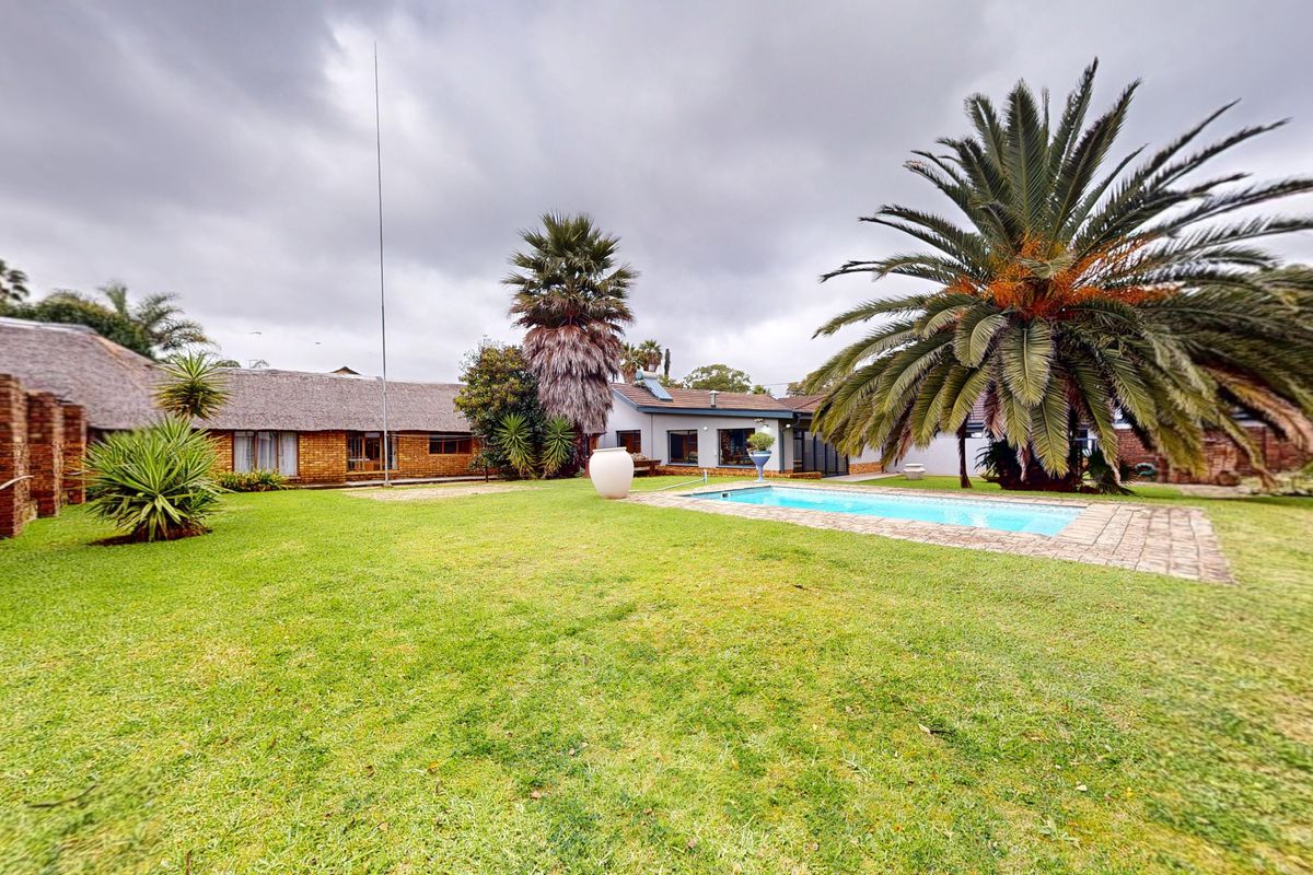 Spacious rear garden featuring a swimming pool, brick-paved surround, and a house with a traditional thatched roof and brick exterior.