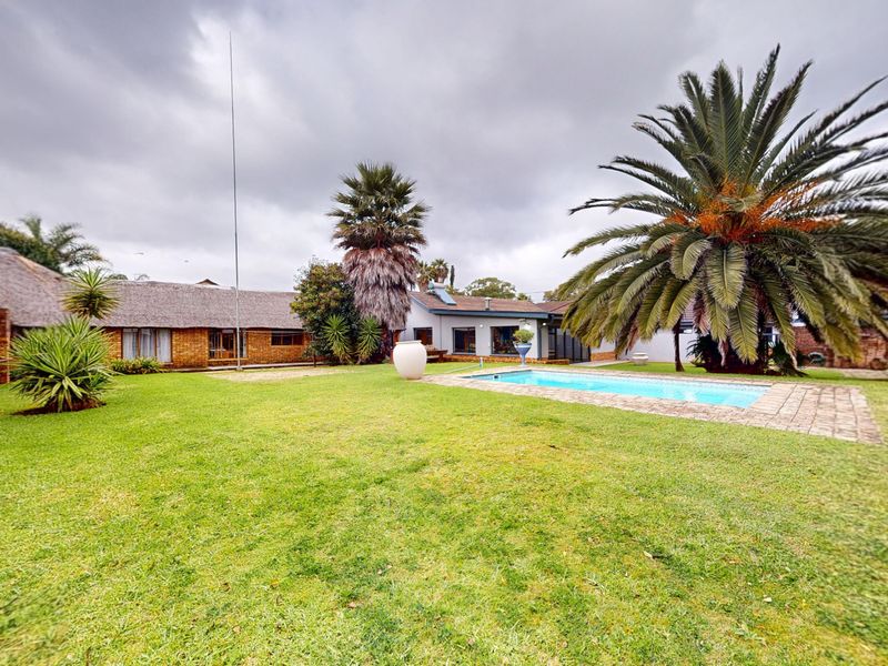 Spacious rear garden featuring a swimming pool, brick-paved surround, and a house with a traditional thatched roof and brick exterior.