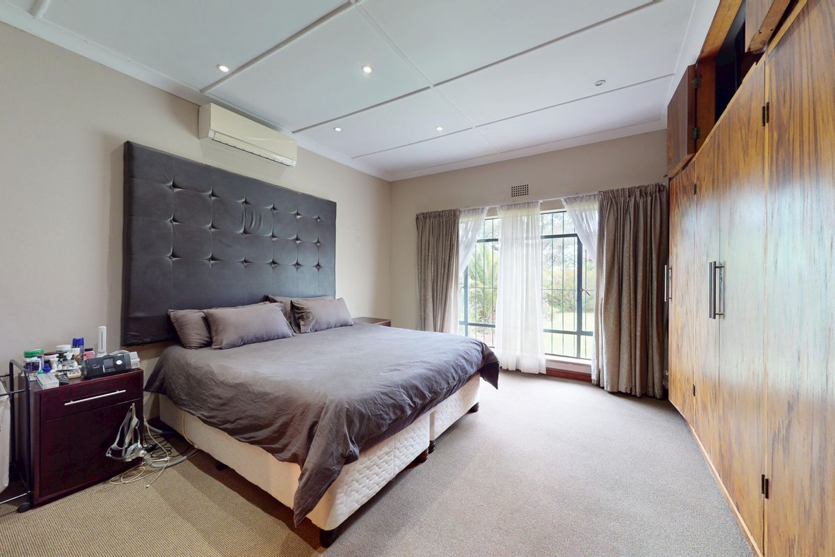 Spacious bedroom featuring built-in wooden cupboards, carpeted flooring, recessed lighting, and a wall-mounted air conditioning unit.