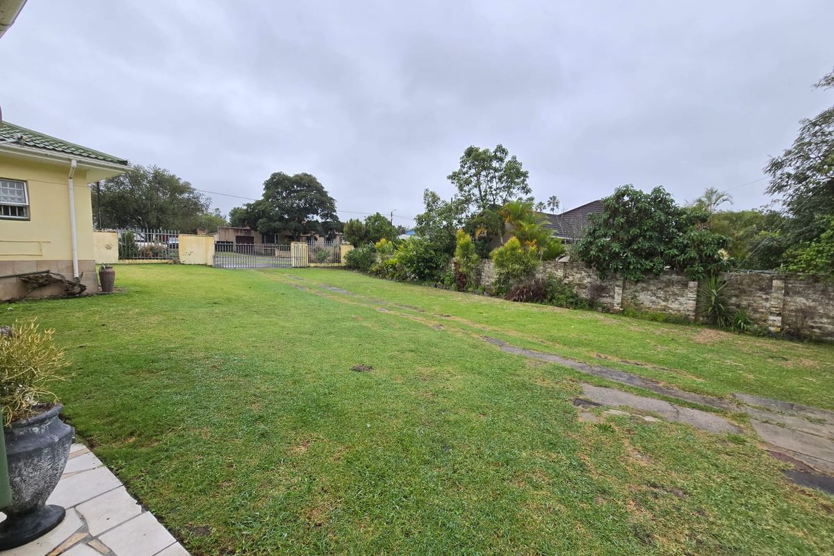 A spacious rear garden featuring a large lawn, stone boundary wall, and paved patio area, providing ample outdoor space.