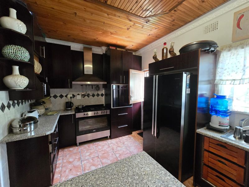 A functional kitchen featuring dark cabinetry, granite countertops, stainless steel appliances, and a distinctive timber tongue and groove ceiling.