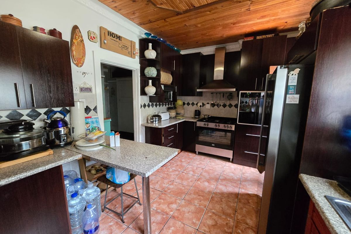 A functional kitchen featuring dark wood cabinetry, granite countertops, a built-in oven with gas hob, and a distinctive timber ceiling.
