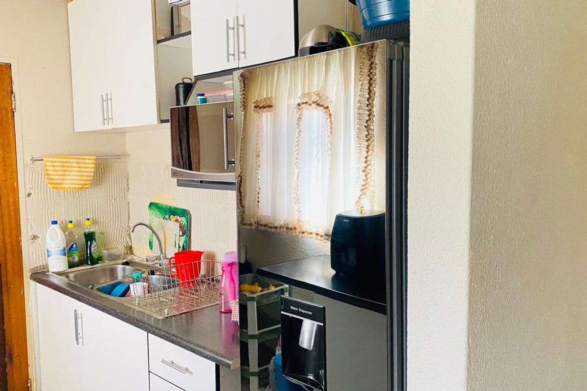 A compact kitchen area featuring white cabinetry, laminate countertops, and a stainless steel sink, requiring minor wall repairs and cosmetic updates.