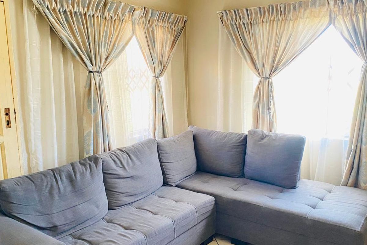 A cozy living room area featuring tiled flooring and natural light through dual windows.
