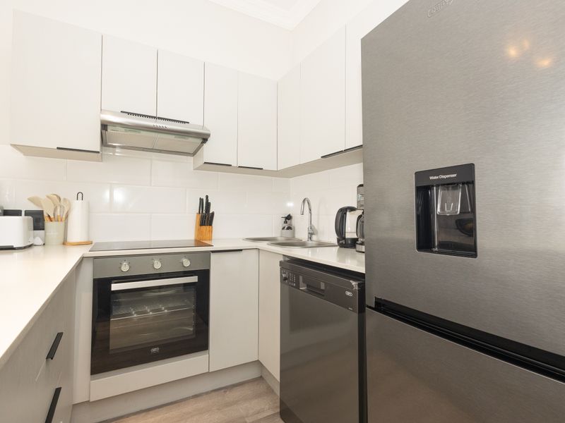 Modern kitchen featuring white cabinetry, stone countertops, subway tile backsplash, and integrated stainless steel appliances including an oven, hob, and extractor fan.