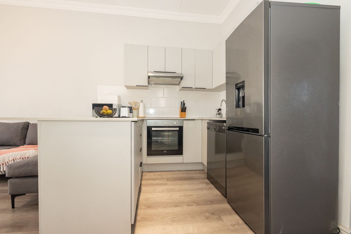 Modern kitchen featuring white cabinetry, subway tile backsplash, built-in oven, extractor fan, and a functional island, seamlessly integrated into the living space.