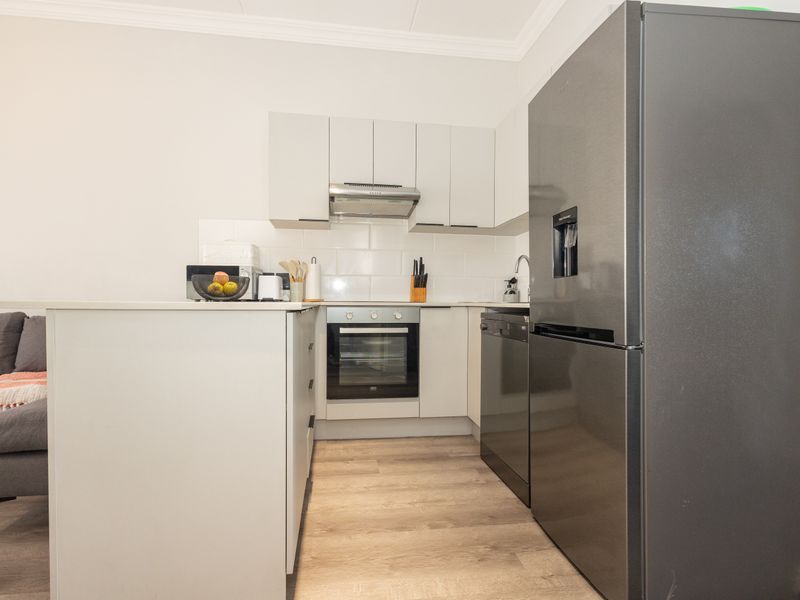 Modern kitchen featuring white cabinetry, subway tile backsplash, built-in oven, extractor fan, and a functional island, seamlessly integrated into the living space.