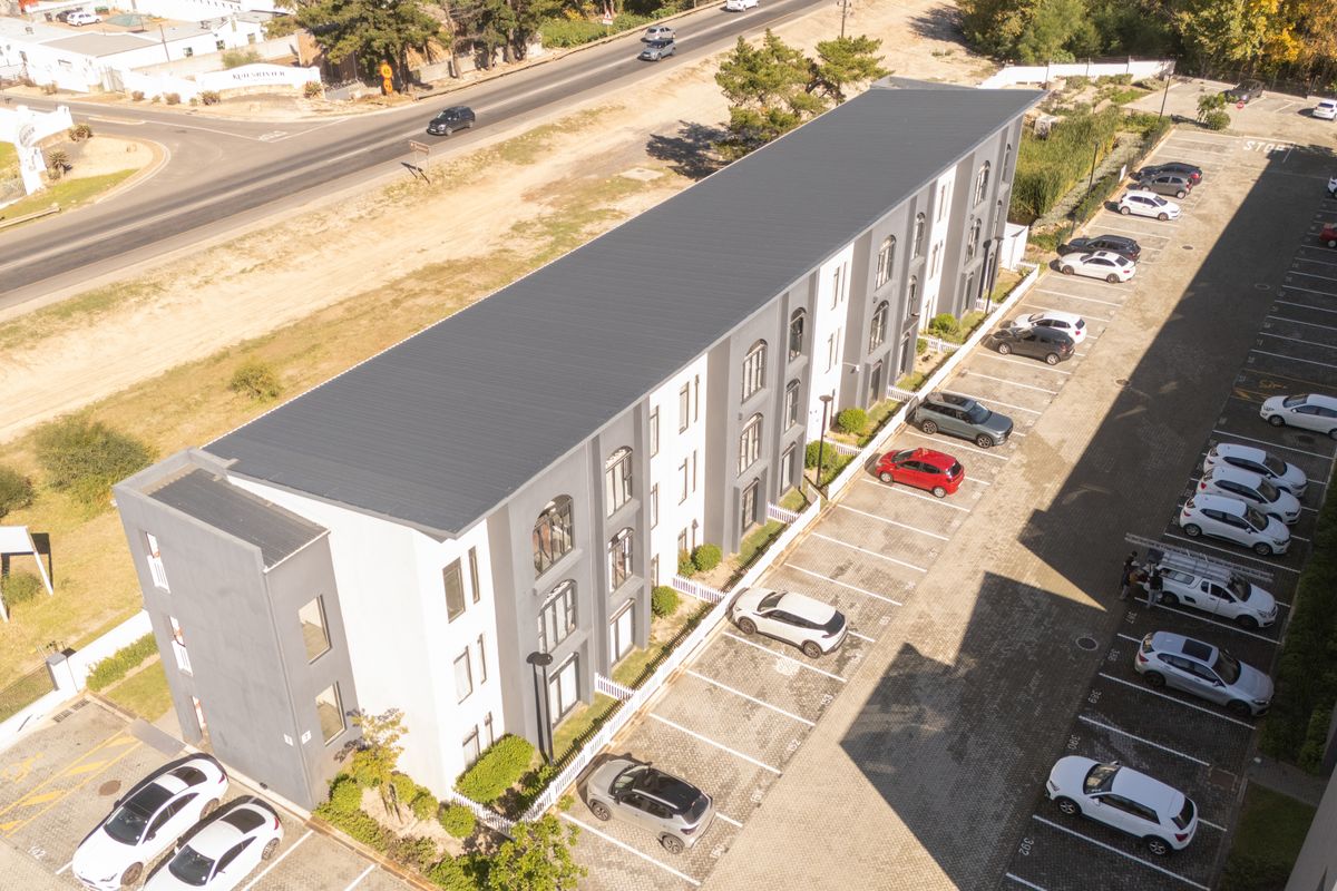 Aerial view of a modern multi-story apartment complex featuring a metal roof and dedicated paved parking bays.
