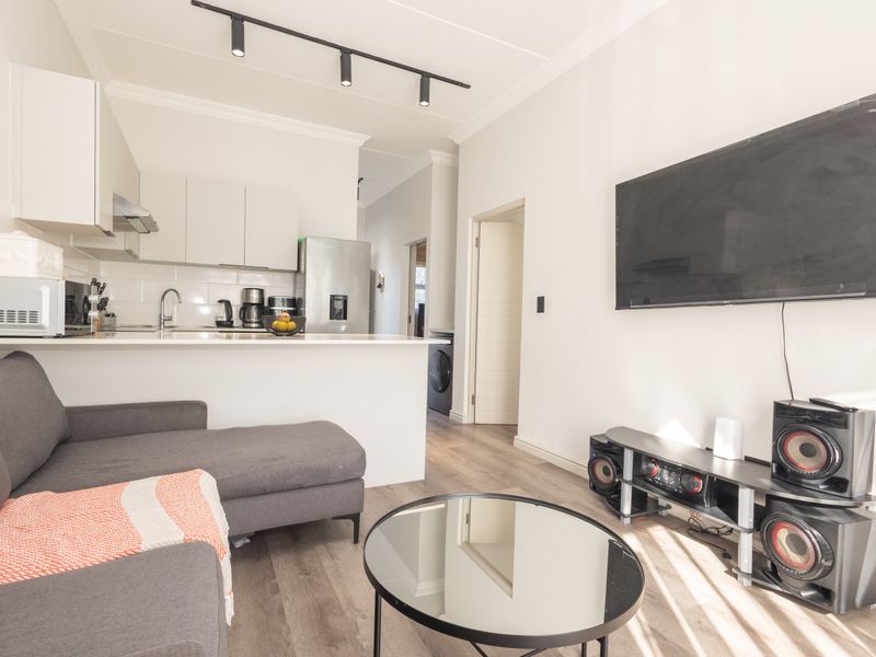 Modern open-plan living area featuring a sleek kitchen with integrated cabinetry, track lighting, and durable laminate flooring throughout the space.
