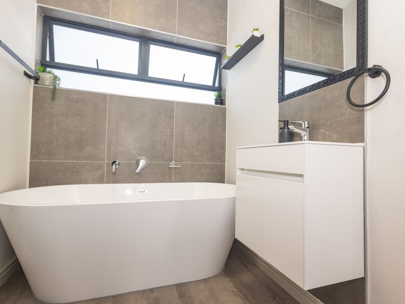 Modern bathroom featuring a sleek freestanding bathtub, wall-mounted fixtures, a contemporary vanity cabinet, and stylish grey wall tiling.
