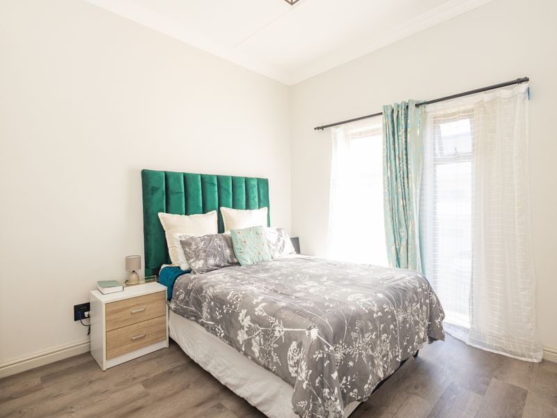 A well-maintained bedroom featuring modern laminate flooring, neutral walls, and a built-in cupboard, offering a bright and comfortable living space.
