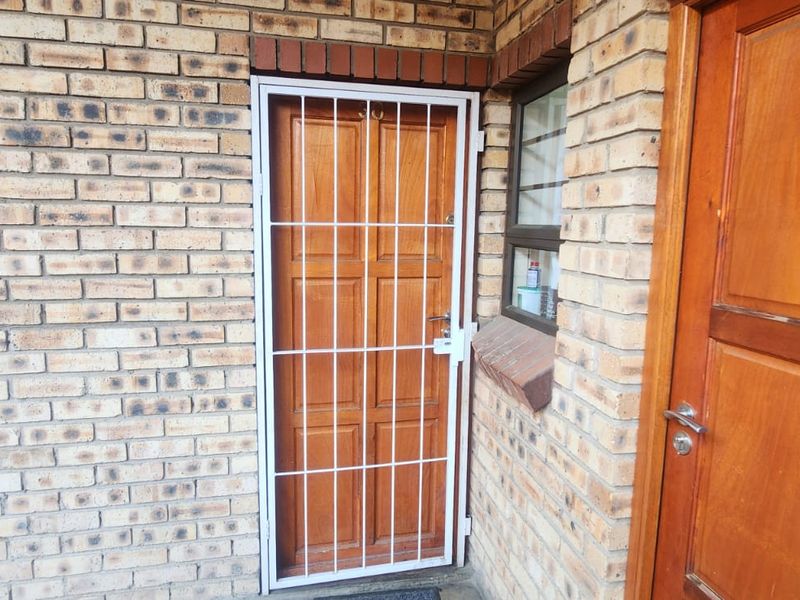 Exterior entrance area featuring face brick walls and multiple timber panel doors with a security gate.